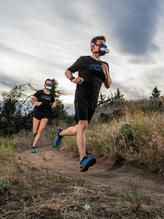 Man and woman running outside while wearing athletic performance analyzer masks to measure their VO2 max scores